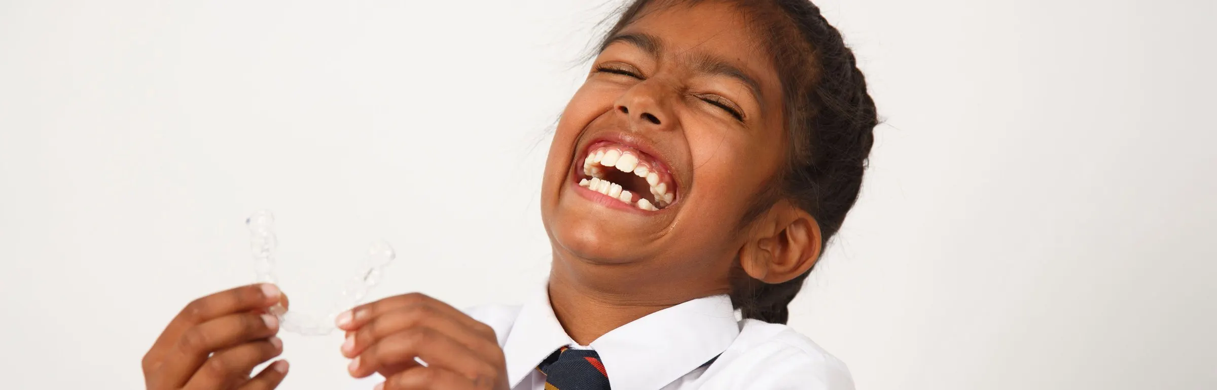 A boy in school uniform laughing and holding his clear aligners