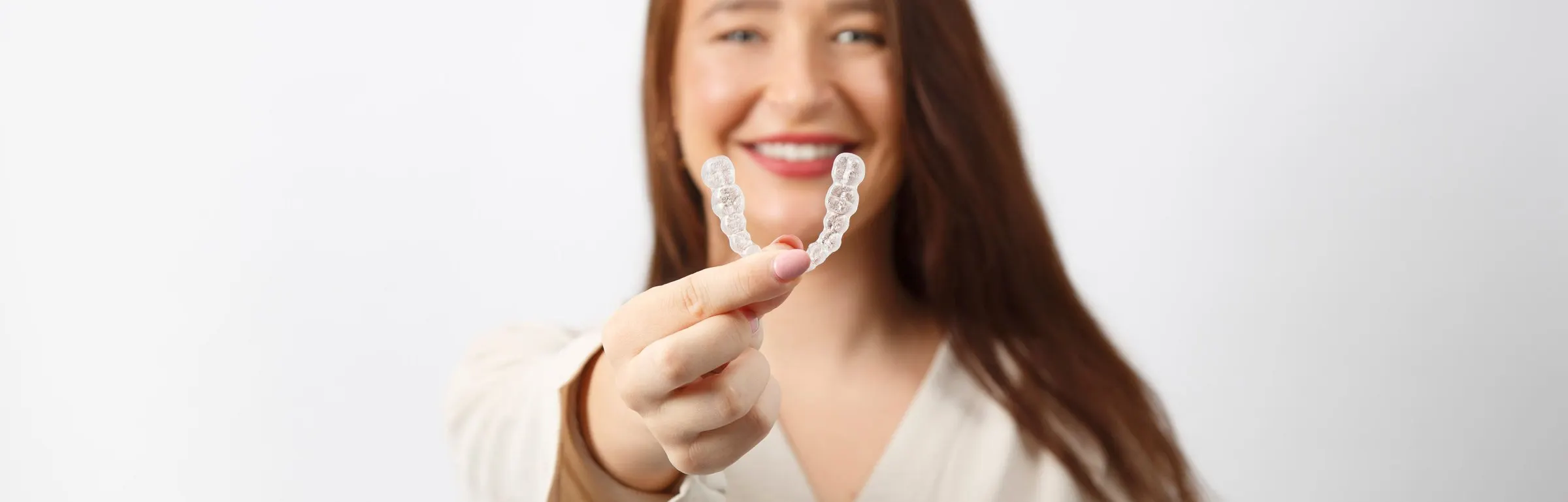 A patient in a green shirt holding her clear aligner up to the camera