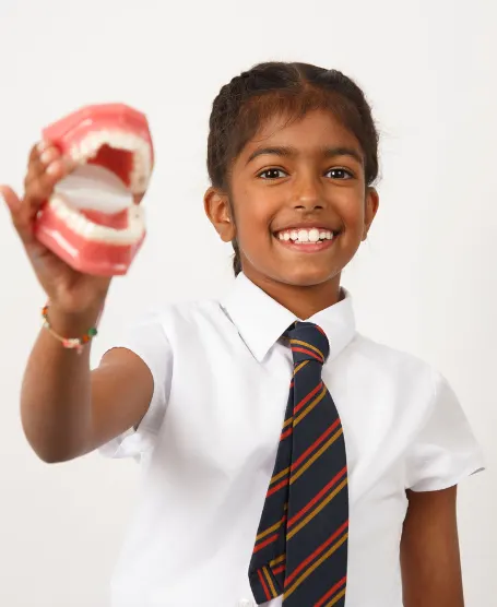 A boy in school uniform holding up a dental model and smiling