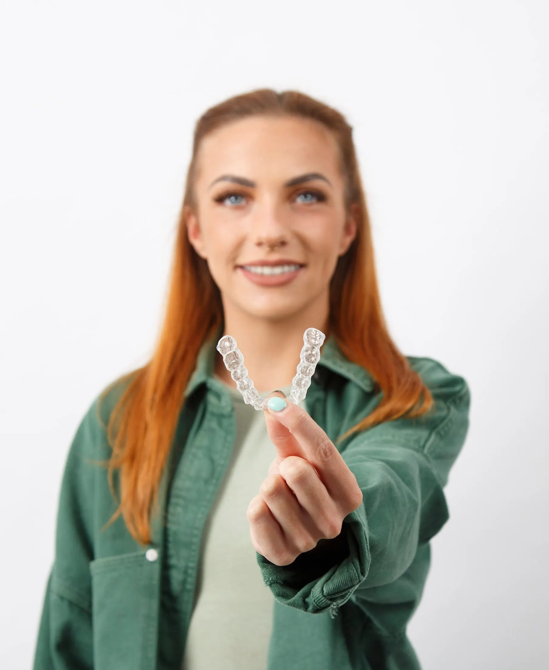 A patient in a green shirt smiling and holding her clear aligner