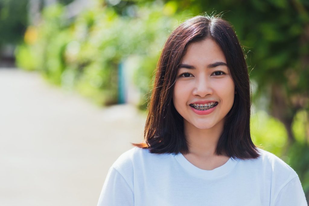 Smiling teenager wearing fixed metal braces on their teeth